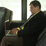 Man in Suit sitting in comfortable bus leather seat using laptop with WiFi